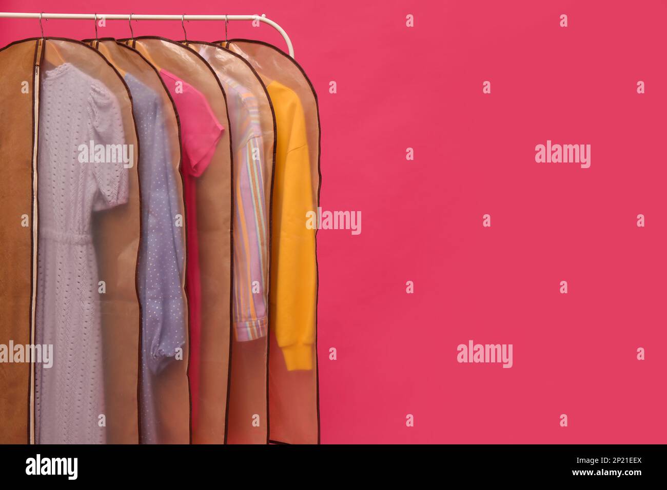 Garment bags with clothes on rack against pink background. Space for ...