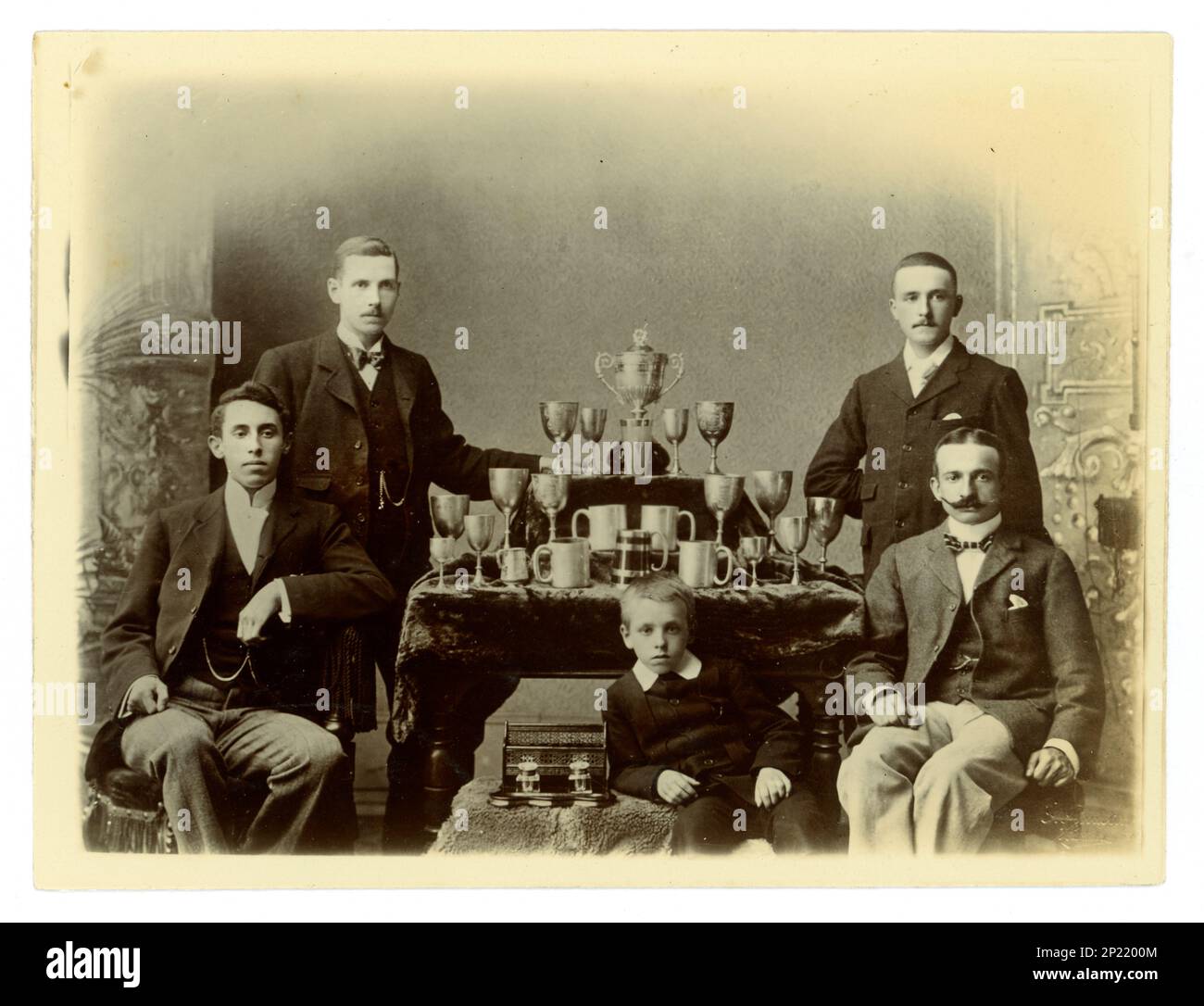 Original Victorian photograph group portrait of gents and a child.  On a table there is displayed a large Worcester challenge vase, / regatta trophy for rowing, and other cups, Possibly members of a coxed four crew. Worcester area, U.K.  circa 1897-1899. Stock Photo