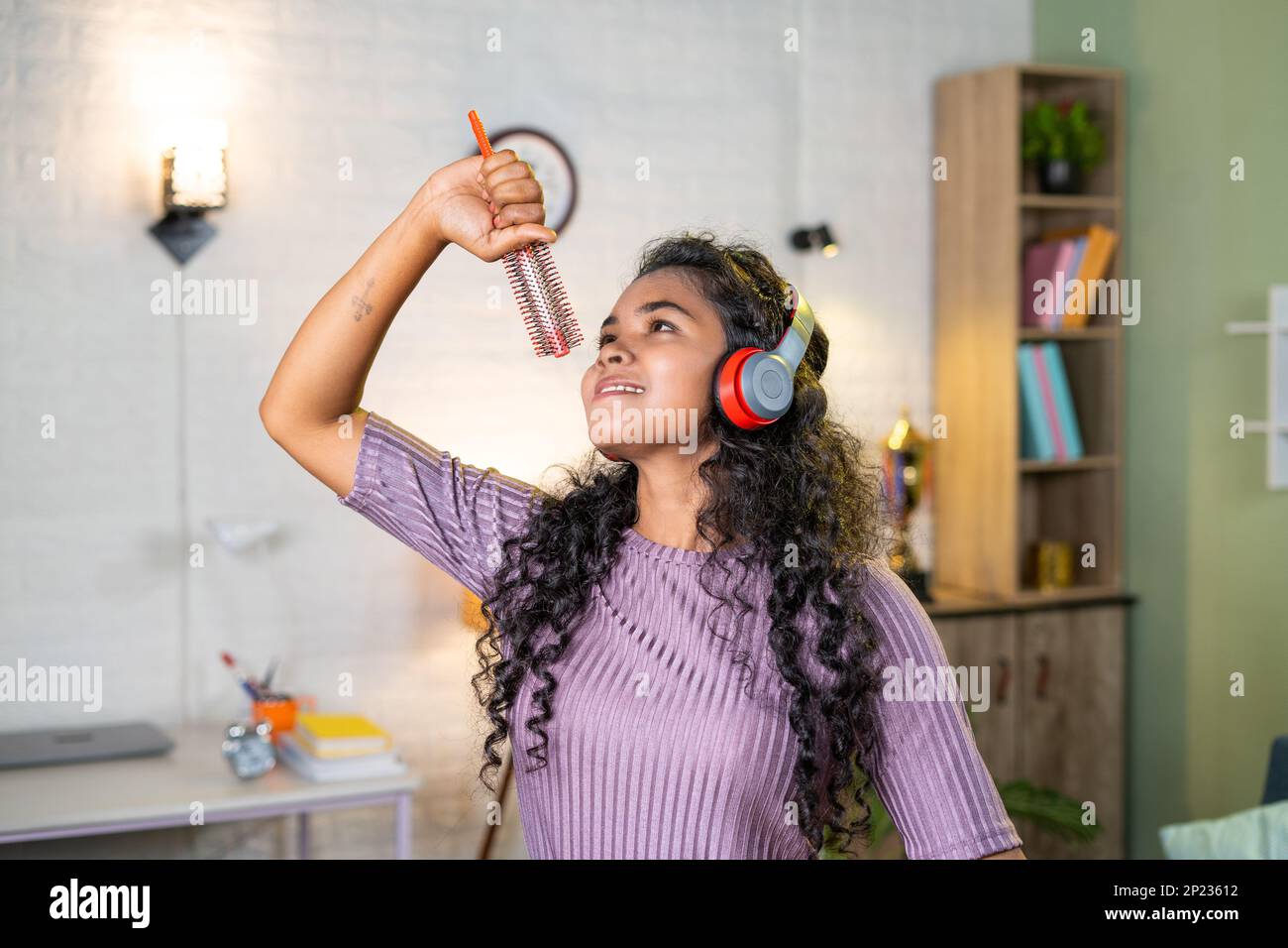 Cheerful girl with wireless headset dancing by singing with hair comb at home - concept of entertainment, freedom and happiness Stock Photo