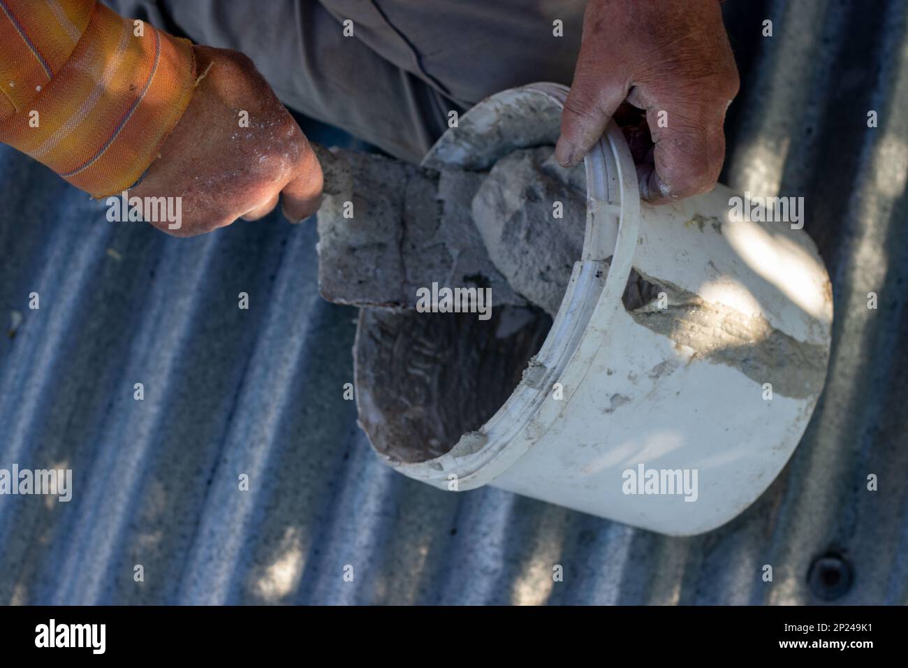 A man is sitting on the roof and filling the bucket with cement mortar. selective focus Stock Photo