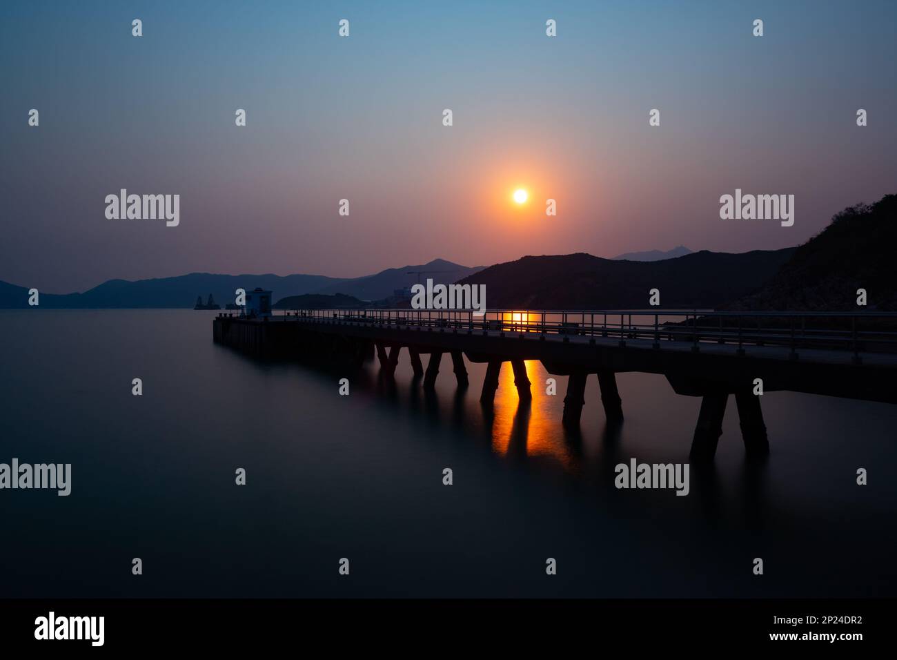 Pier at sunset.  Long exposure, smooth sea, orange sun reflection. Stock Photo