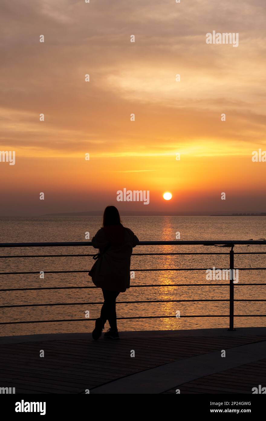 Person standing alone on a pier enjoying dramatic sunset at the sea. Stock Photo
