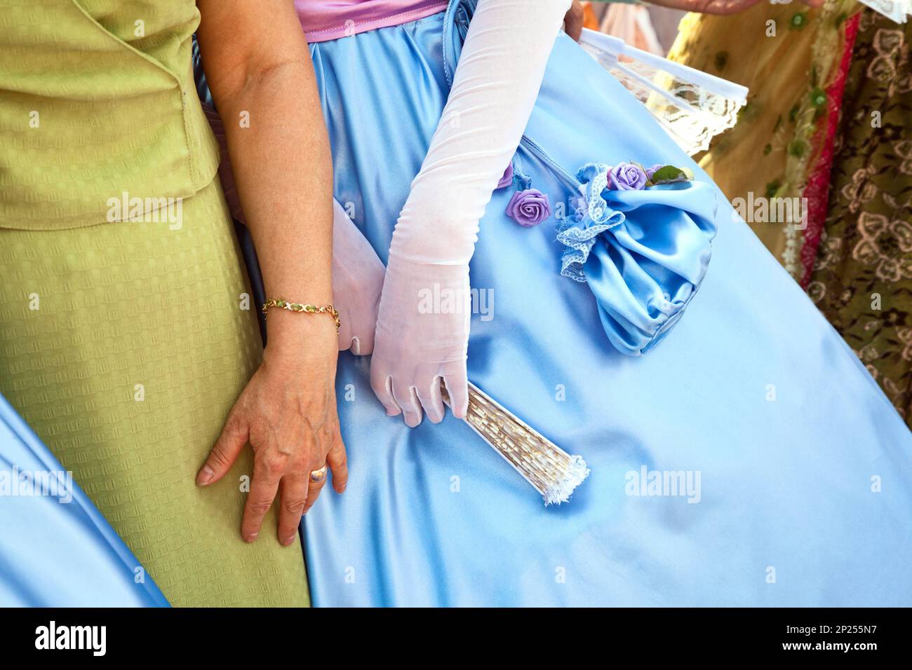 Two ladies wearing bright blue and green formal dresses. Historical female costumes and accessories - fan,  purse, gloves - in a role-play Stock Photo