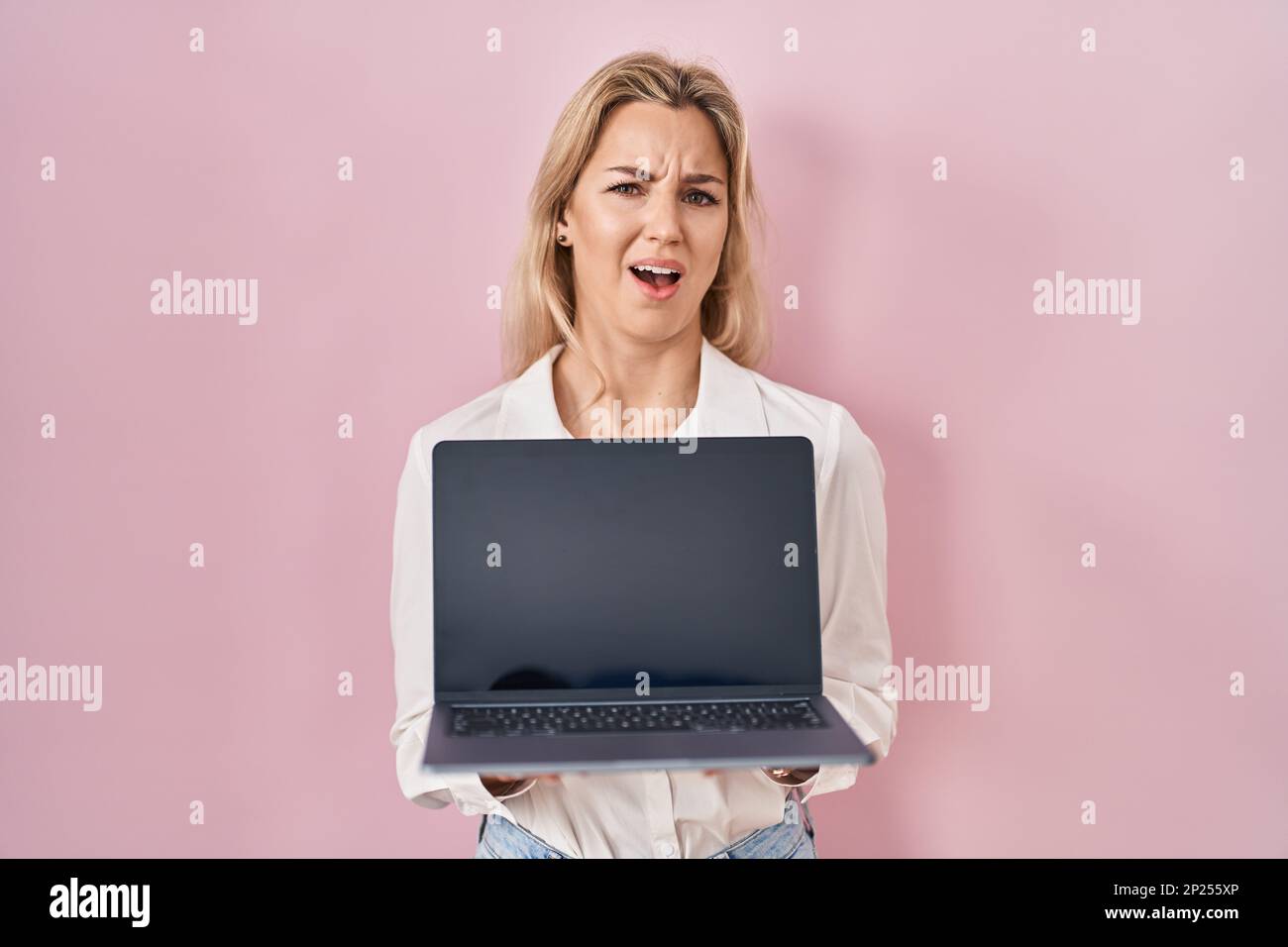 Young caucasian woman holding laptop showing screen clueless and ...