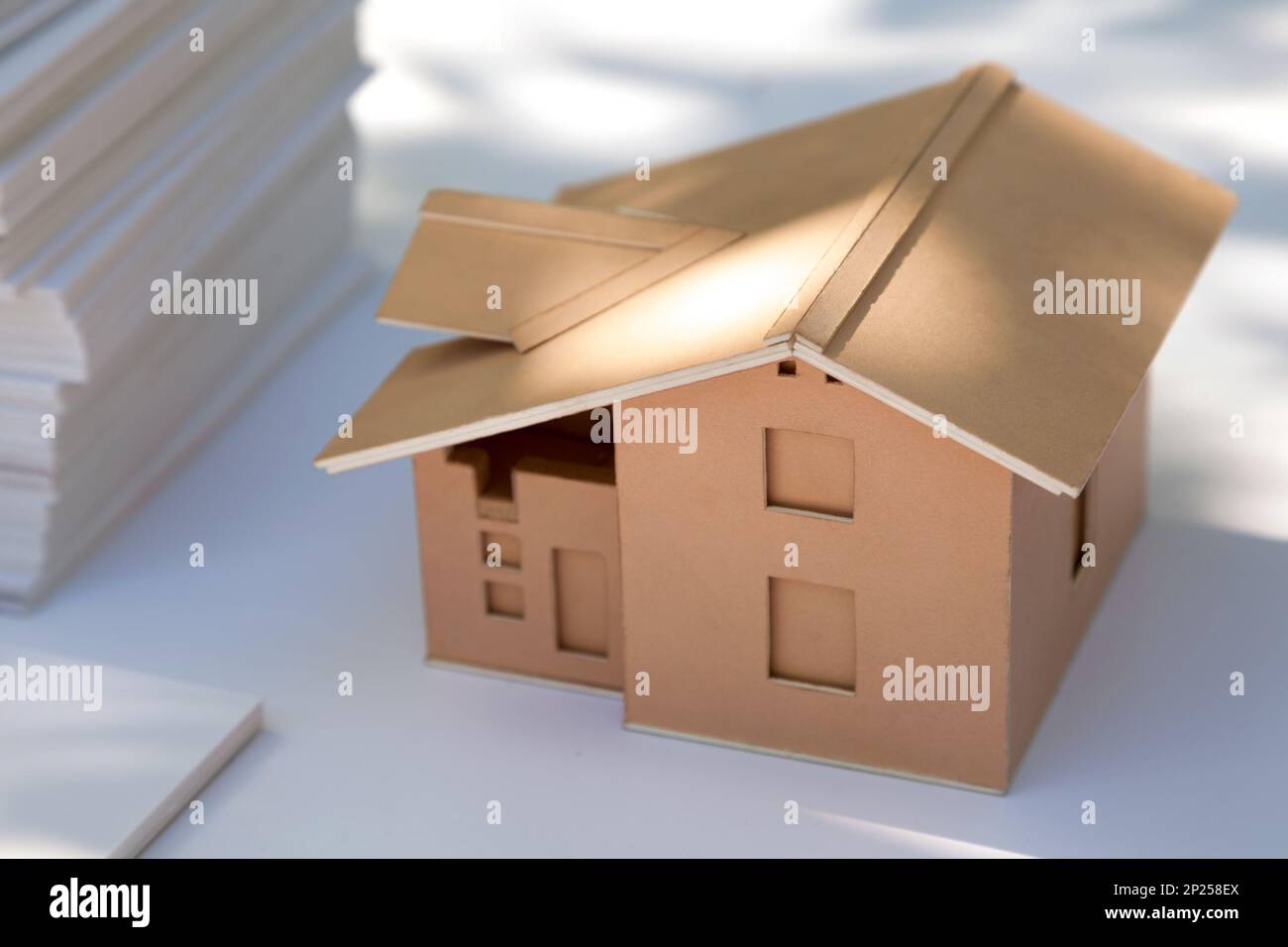 Small cardboard house model on white. New home design for sale. Abstract cardboard real estate miniature in the sunlight Stock Photo
