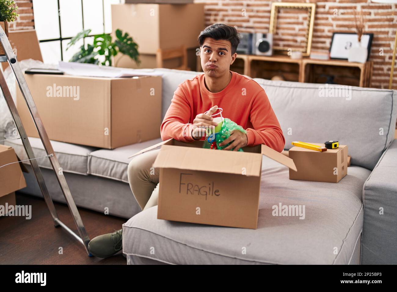 Hispanic man moving to a new home unpacking puffing cheeks with funny ...