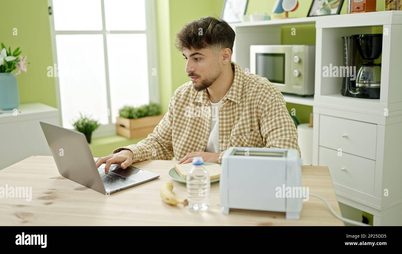 Young arab man having breakfast using laptop at home Stock Photo
