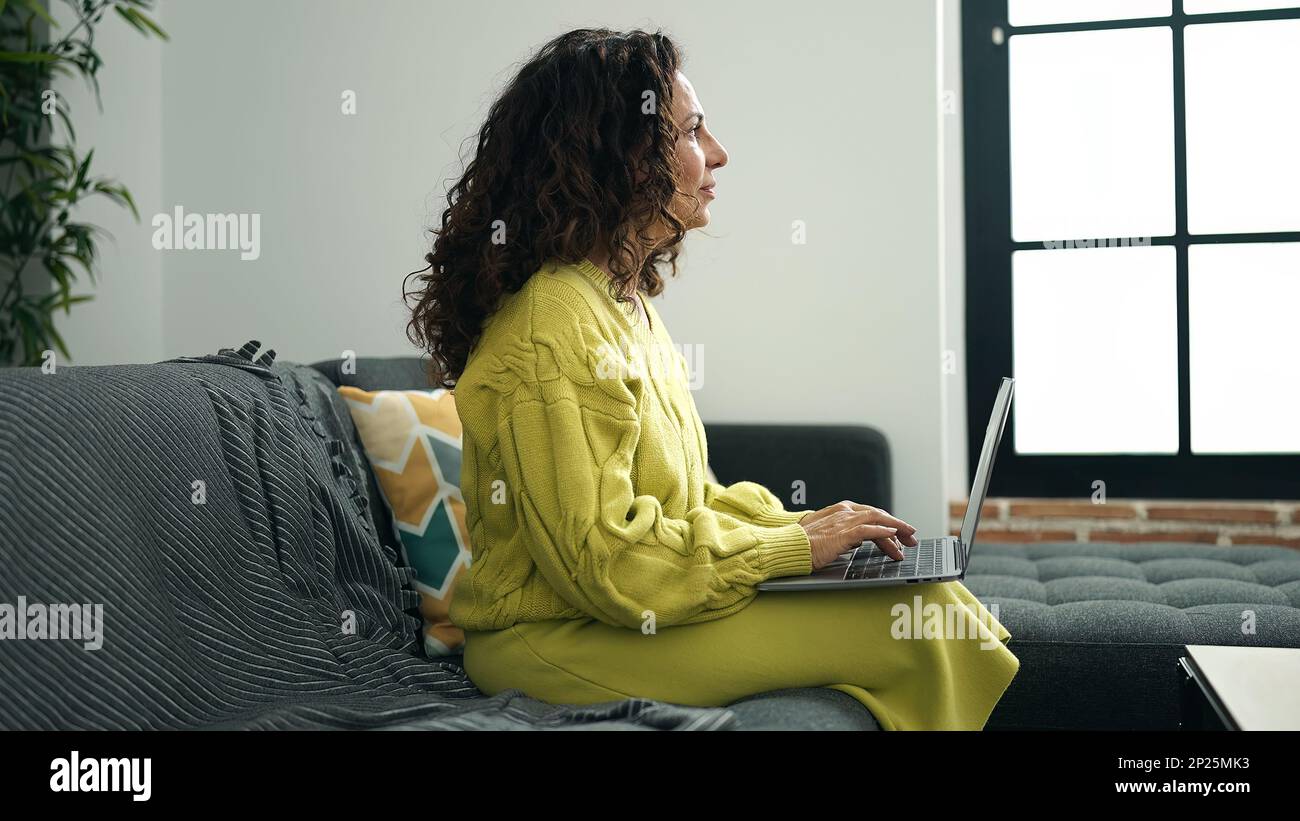 Middle age hispanic woman using laptop sitting on sofa at home Stock ...