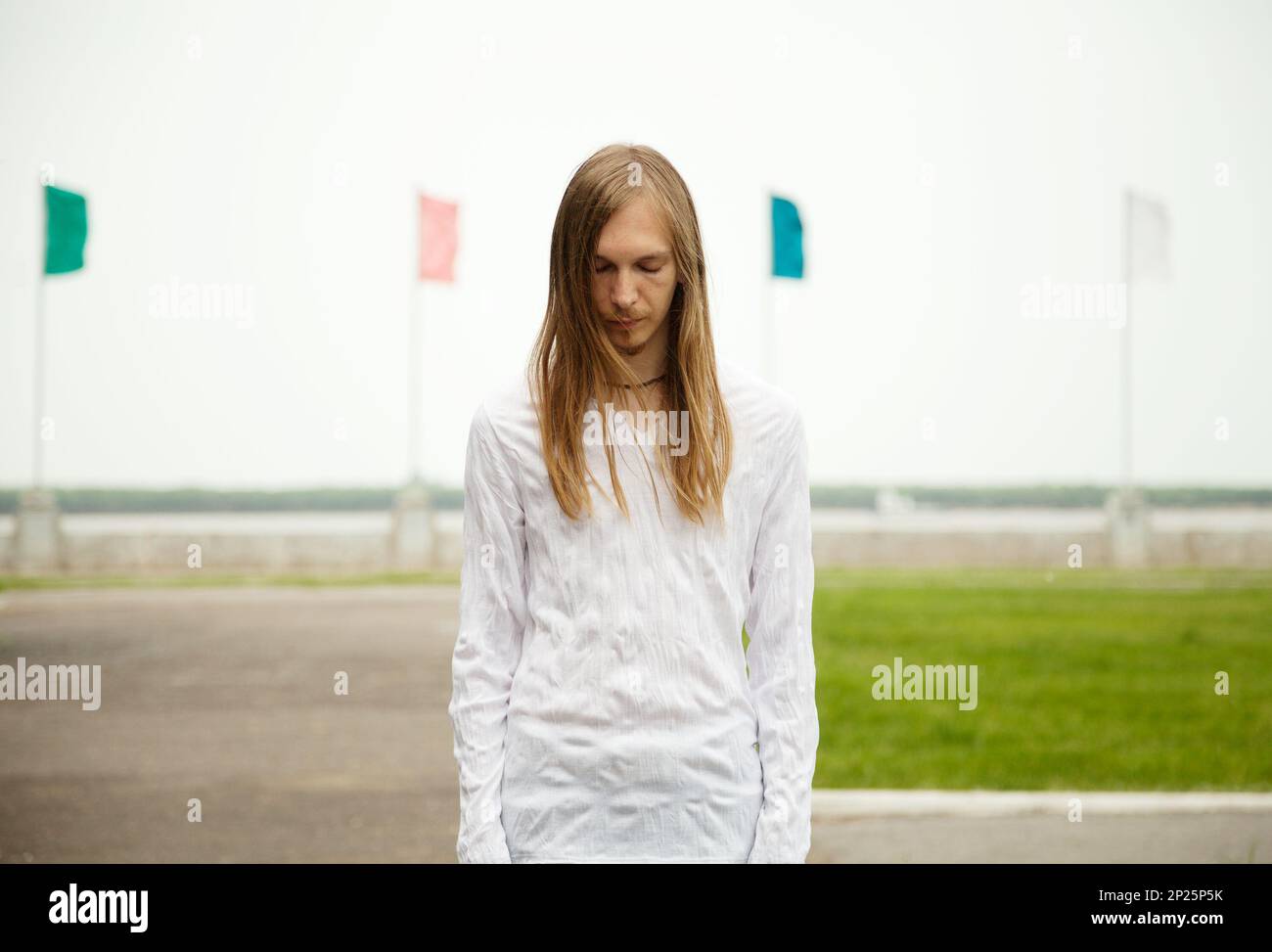 Young white man standing at the park with sad face and closed eyes. Peaceful tranquil scene with a person meditating outdoors Stock Photo