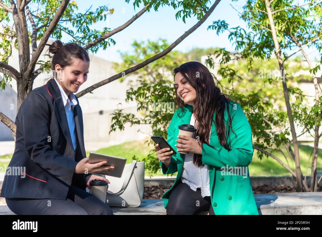 Co-workers using mobile phone and digital tablet while having a coffee break outdoors. Stock Photo