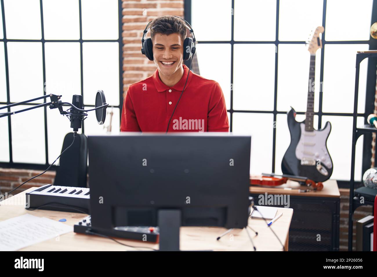 Young hispanic man playing piano keyboard at music studio looking positive and happy standing and smiling with a confident smile showing teeth Stock Photo