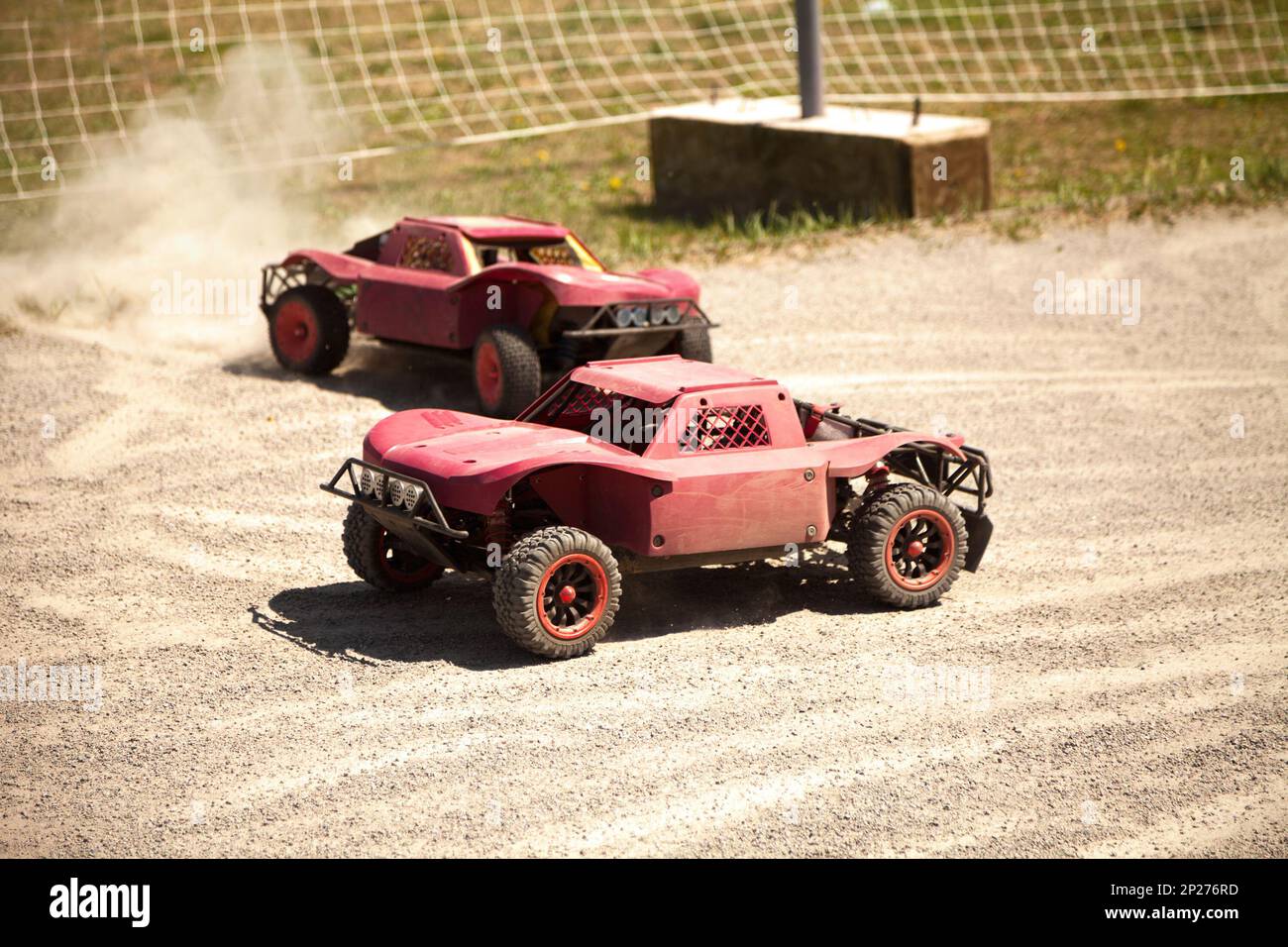 Two small radio controlled model cars racing in the dust. Miniature
