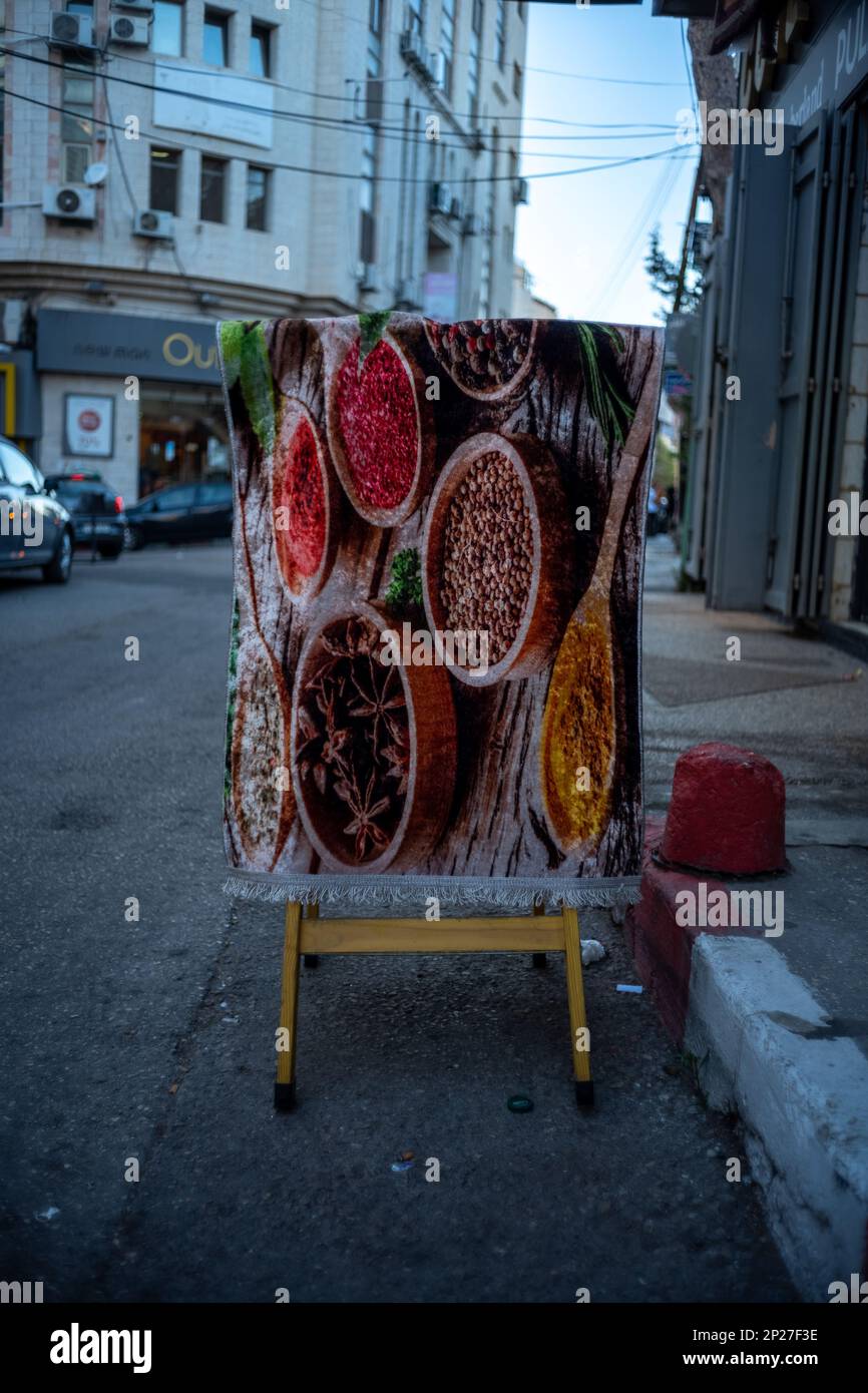 Ramallah, Ramallah and al-Bireh Governorate, Palestine, 8 July 2022: Spice-Themed Carpet Hangs on a Wooden Stand by the Sidewalk in Old Town Street Stock Photo