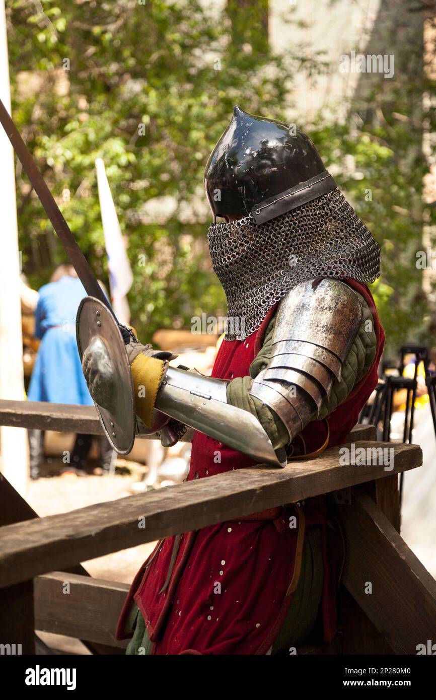 Middle ages period costume at knight tournament. Medieval historical reenactment - a man wearing metal helmet and armor suit, holding a sword Stock Photo