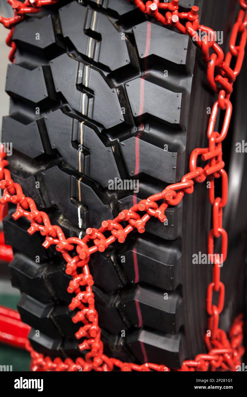 New clean studded tire chains close-up. Black wheel wrapped in red snow chains Stock Photo