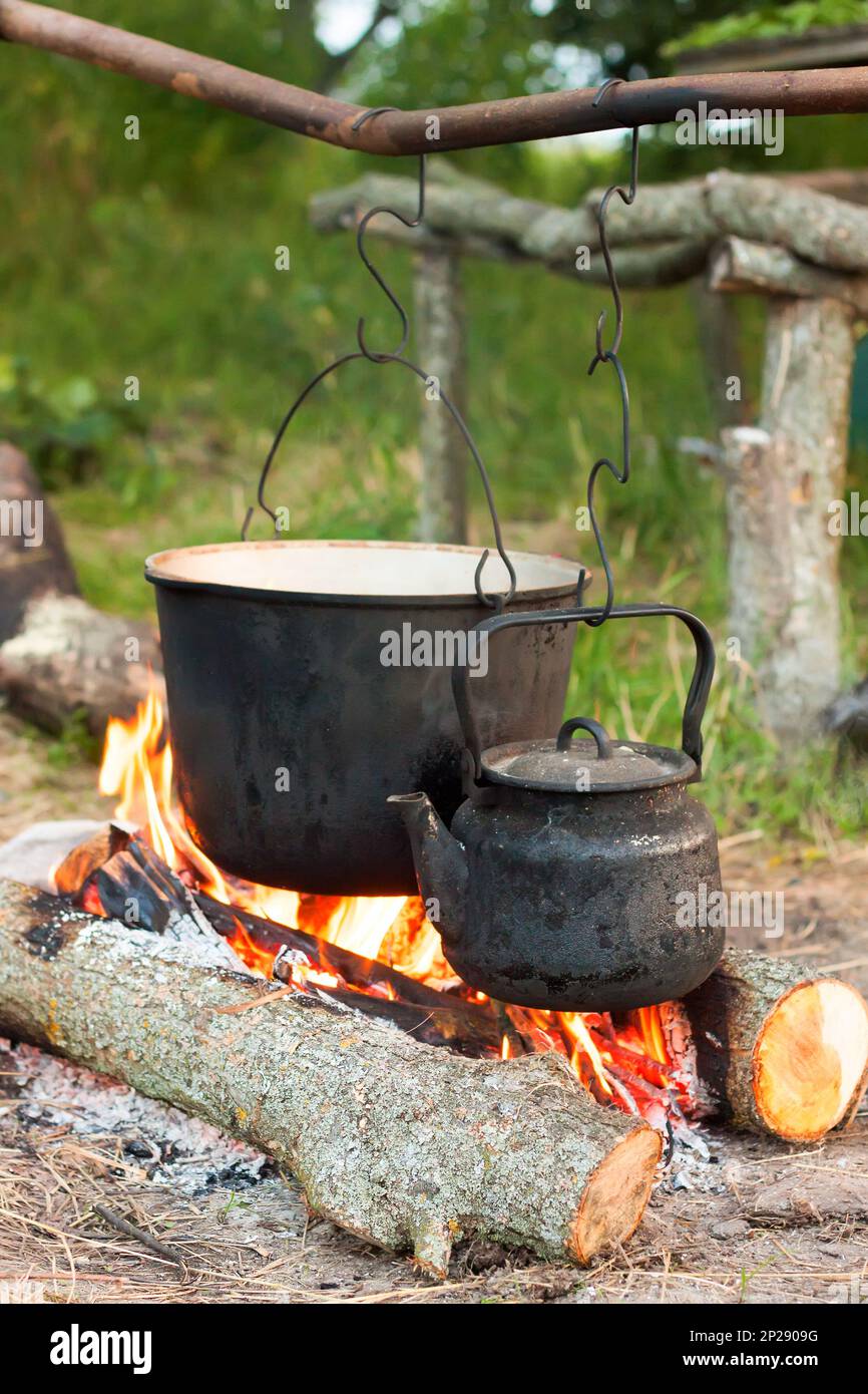Two smoked tourist kettles over camp fire. Process of cooking on the