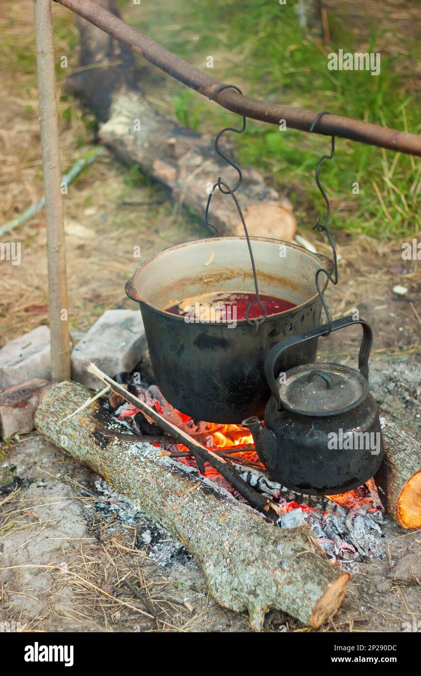 Two smoked tourist kettles over camp fire. Process of cooking on the
