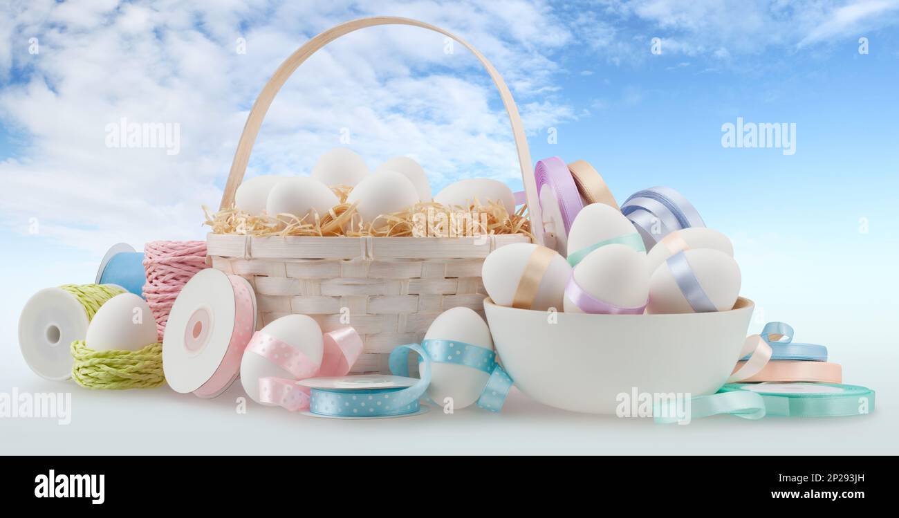 Happy Easter decorations, basket eggs with light pastel colored bright ribbons bows and string, isolated on blue sky background, banner for gift greet Stock Photo