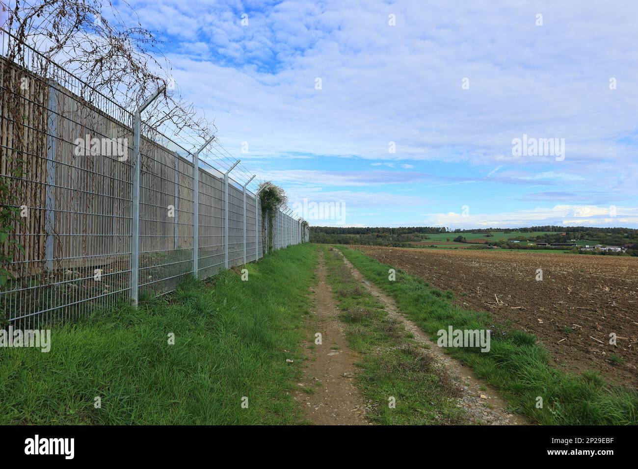 Dirt road runs parallel to the fence of a property Stock Photo