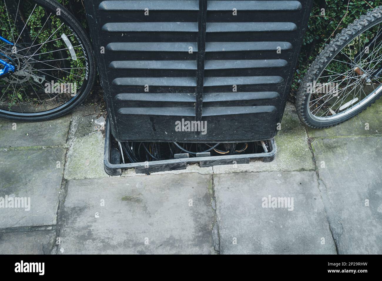 Partially damaged telecom and fibre street cabinet seen on a pavement next to two chained up bicyles in the famous University town. Stock Photo