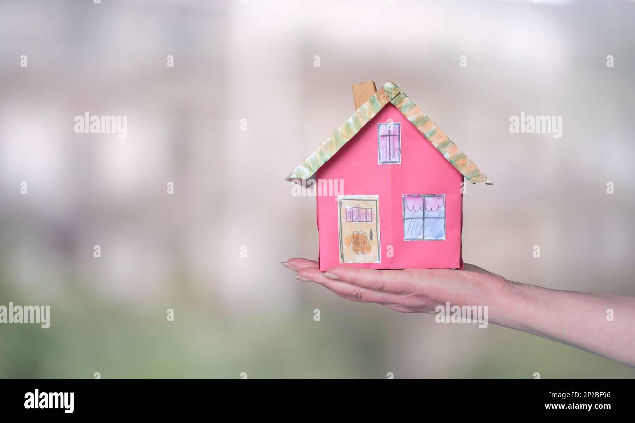 Construction and architecture concept. cute model home on a female hand on blurred buildings background Stock Photo