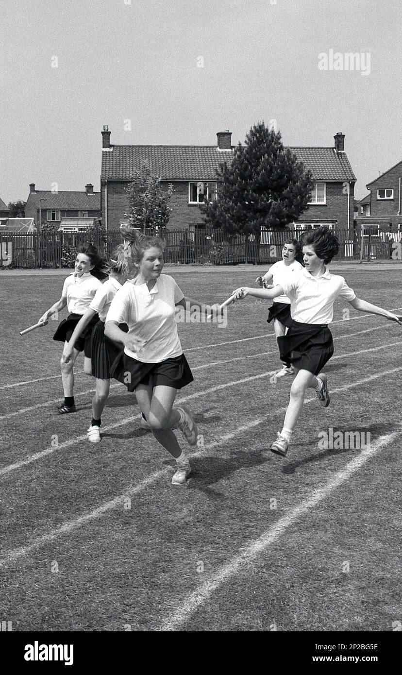 1989, secondary school sports day, outside on a sports field, young teenage girls running in a relay race, handing over the baton to their teammates, England, UK. Stock Photo
