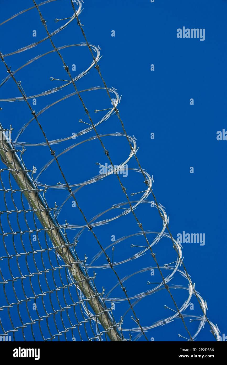 A security fence with razor wire and blue sky Stock Photo - Alamy