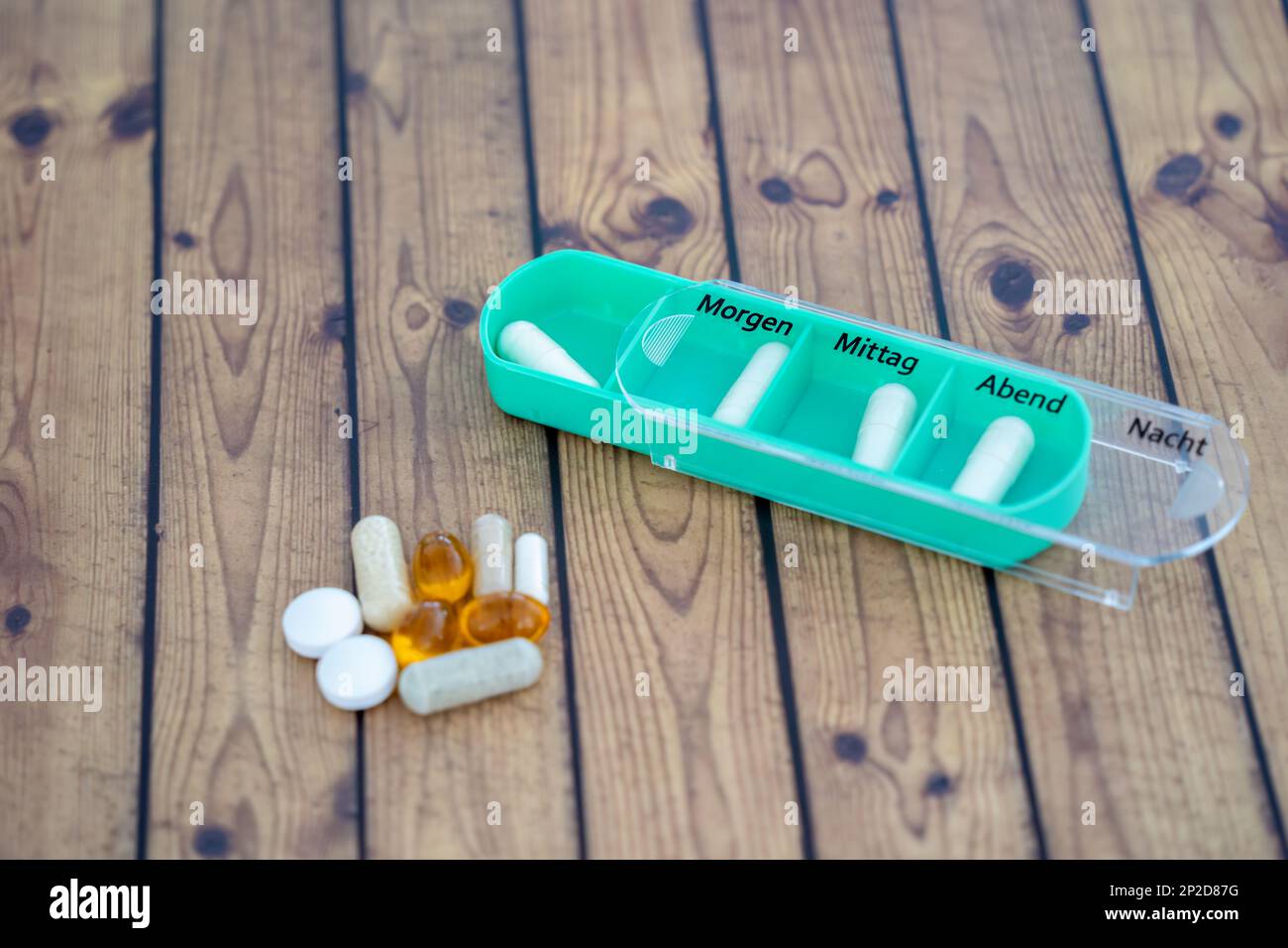 Coloured pill box with four slots, one slot open. Box for one day, german letters Stock Photo