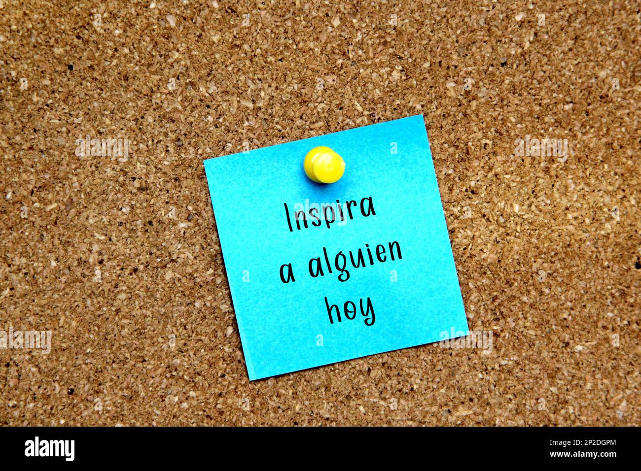 Multicolored notes on cork board with message in Spanish language 'Inspire someone today' Stock Photo