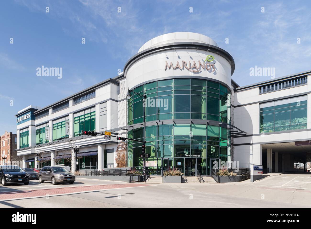 The exterior of a modern exterior, Mariano's grocery store, owned by Kroger, with an entrance to a covered garage and an LA Fitness in the distance. Stock Photo