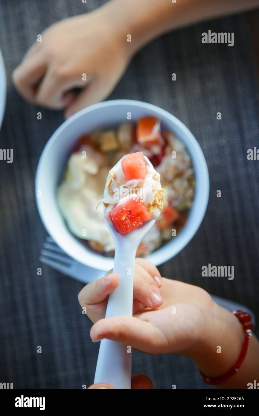 Little girl eating muesli with yoghurt and fruits with white plastic