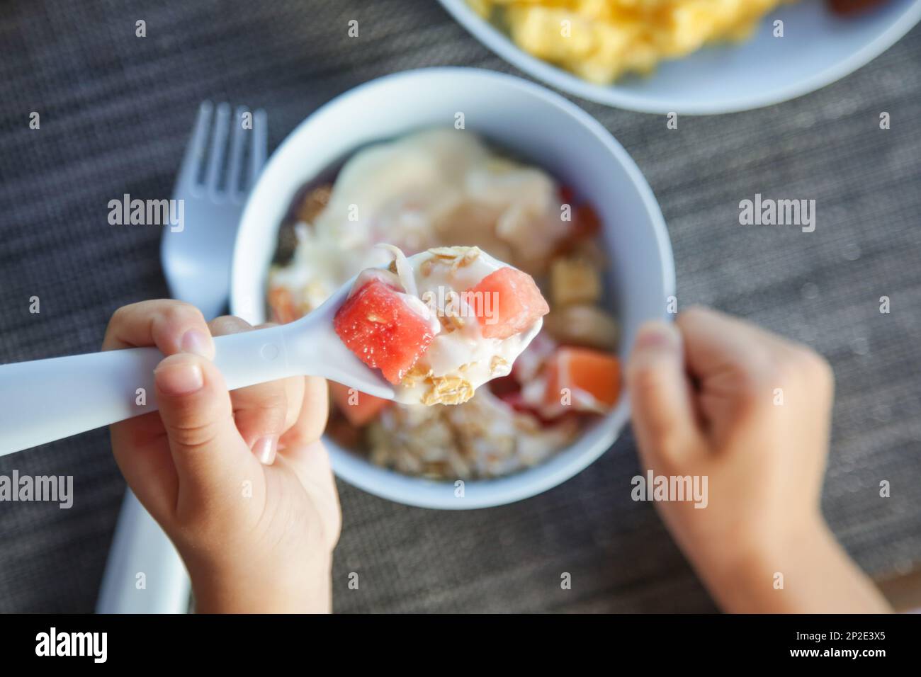 Little girl eating muesli with yoghurt and fruits with white plastic