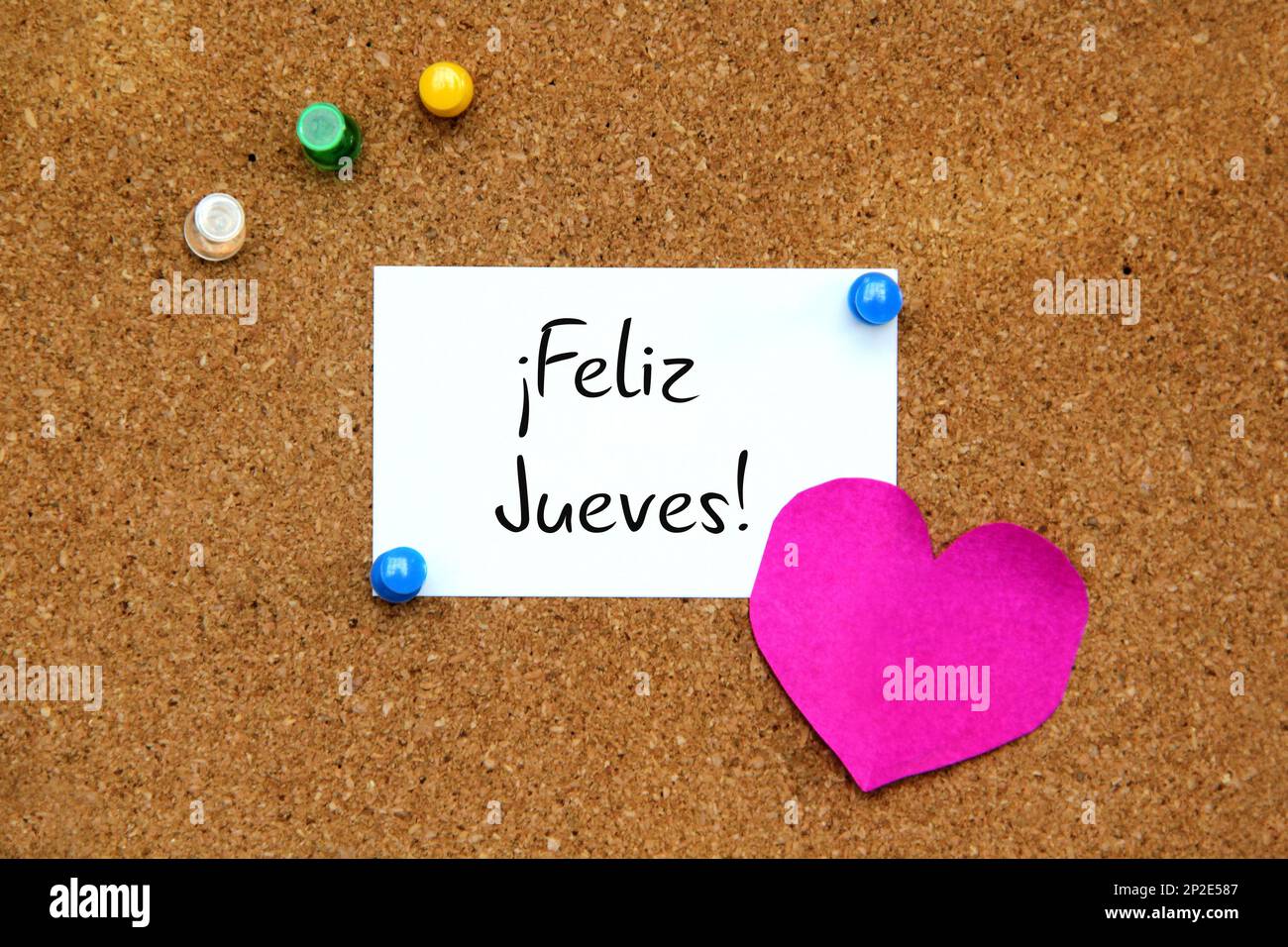 White and colored notes on cork board with message in spanish language "Happy Thursday Stock