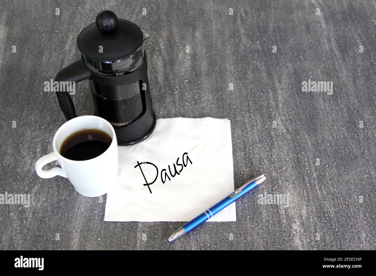 Cup of coffee, French press and white napkin with message in Spanish
