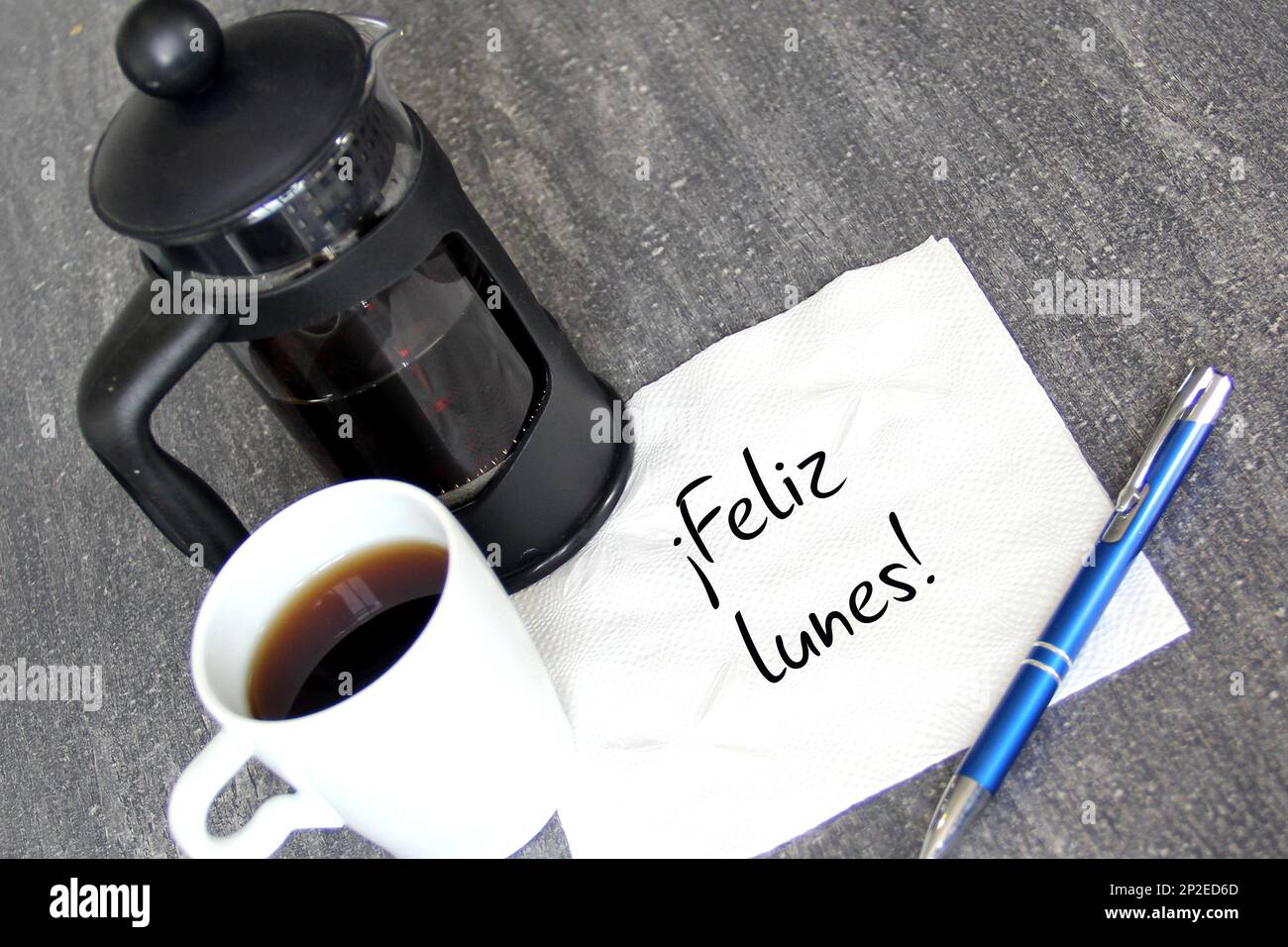 Cup of coffee, French press and white napkin with message in Spanish