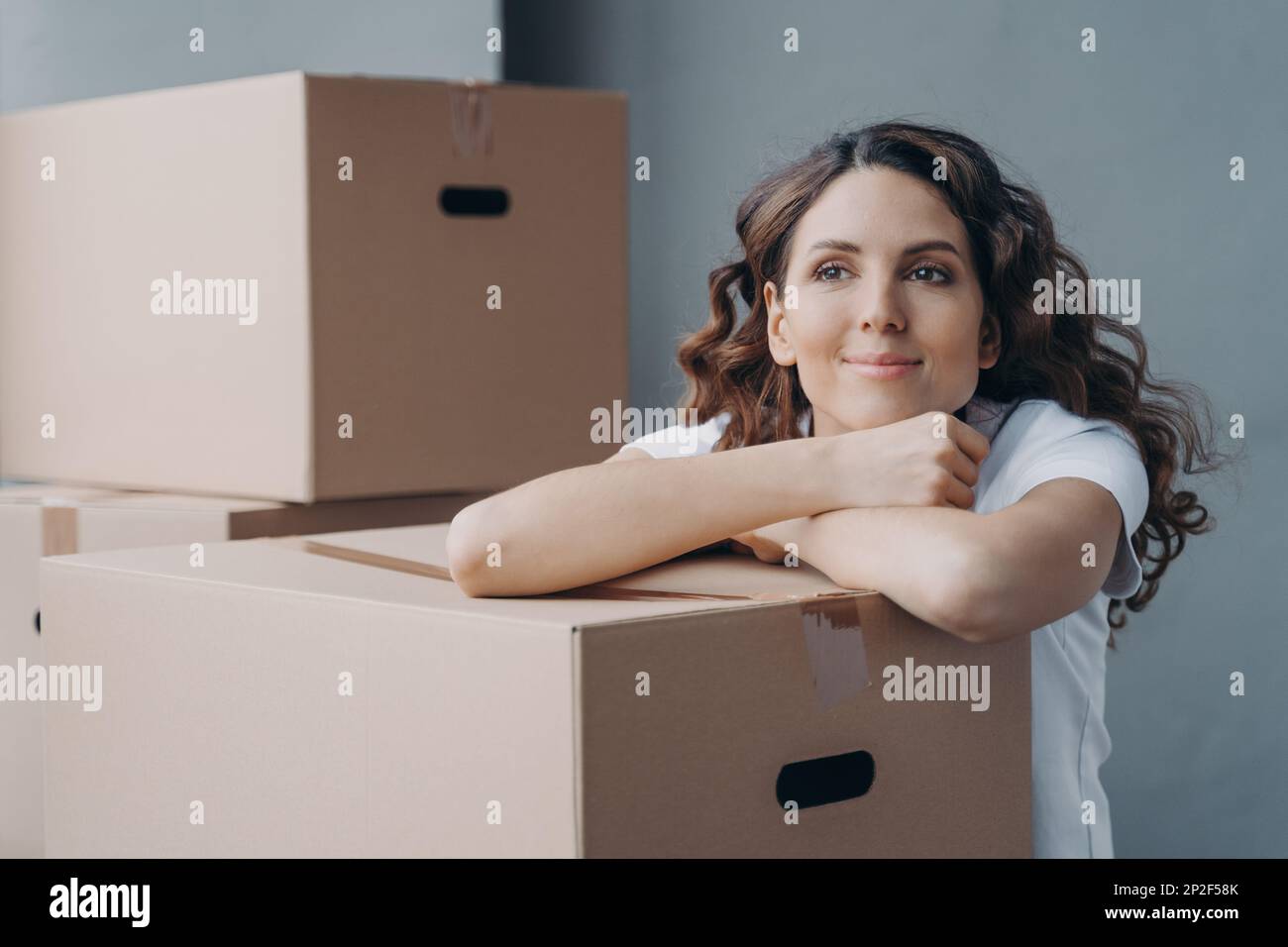Happy satisfied hispanic woman has a break during packing things for relocation. Relaxed female waiting for moving company, dreaming about new home re Stock Photo