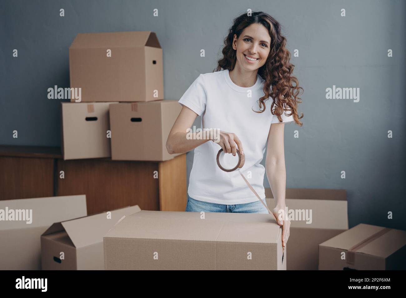 Smiling spanish woman packing stuff in cardboard box, using adhesive