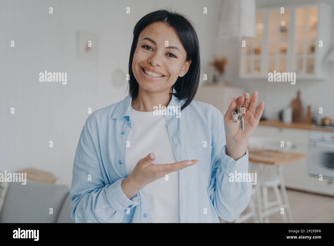 Smiling female tenant or homeowner showing keys to new home. Happy woman renter holding key to apartment, looking at camera. Real estate sale. Rental Stock Photo