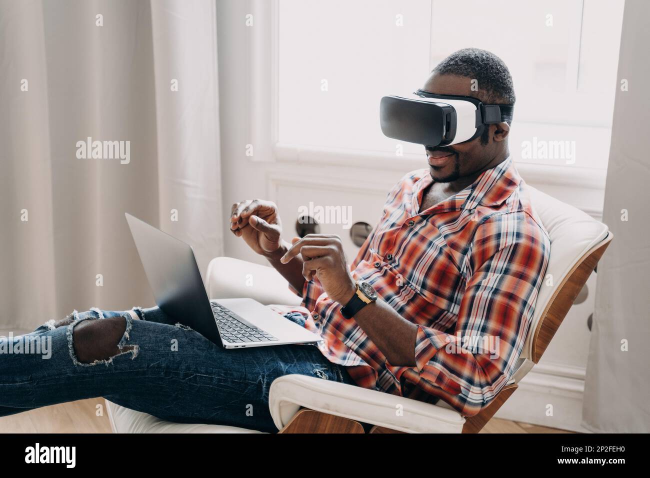 Modern african american man wearing vr glasses working in cyberspace at laptop, black guy developer or designer interacting with virtual reality objec Stock Photo