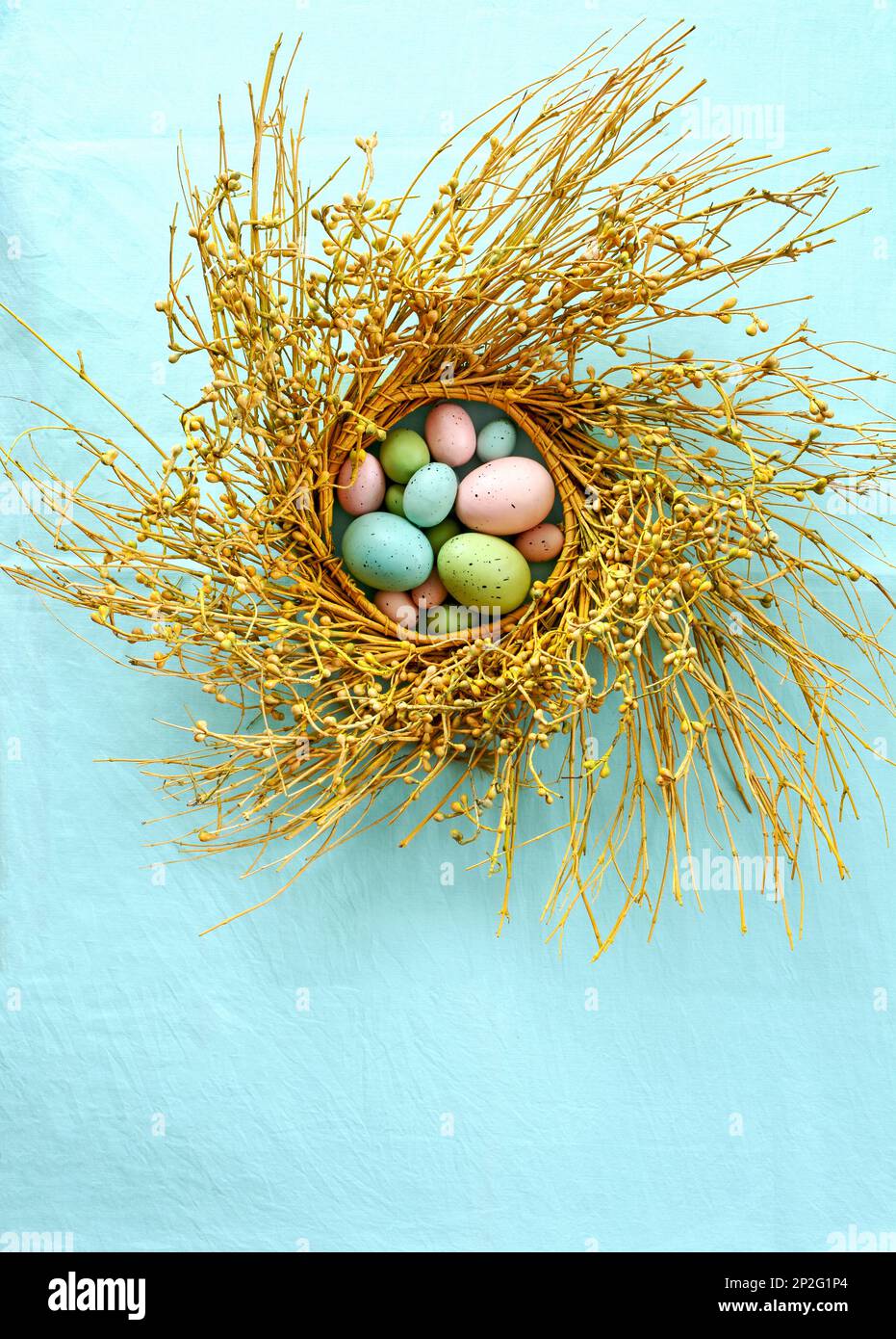 Pastel colored easter eggs in rustic berry branch wreath on turquoise background. Vertical format shot from above in flat lay composition. Stock Photo