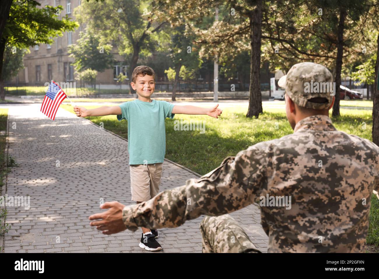 Little boy with flag of USA running towards his father in military uniform outdoors. Family reunion Stock Photo
