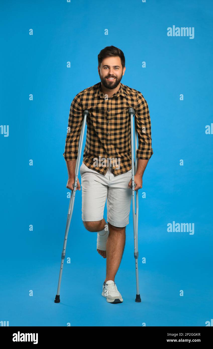 Young man with injured leg using axillary crutches on light blue