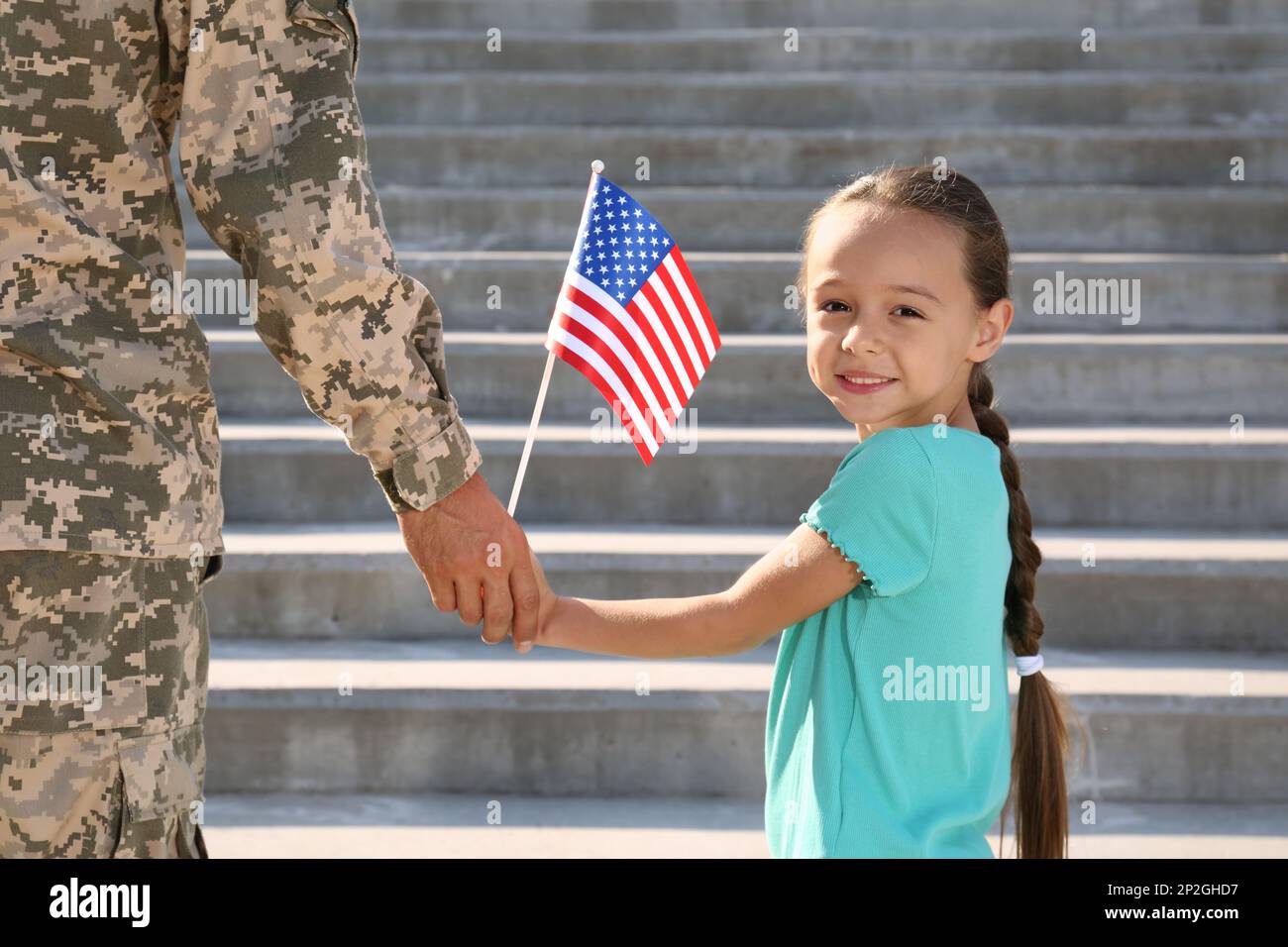 Soldier and his little daughter with American flag holding hands outdoors. Veterans Day in USA Stock Photo