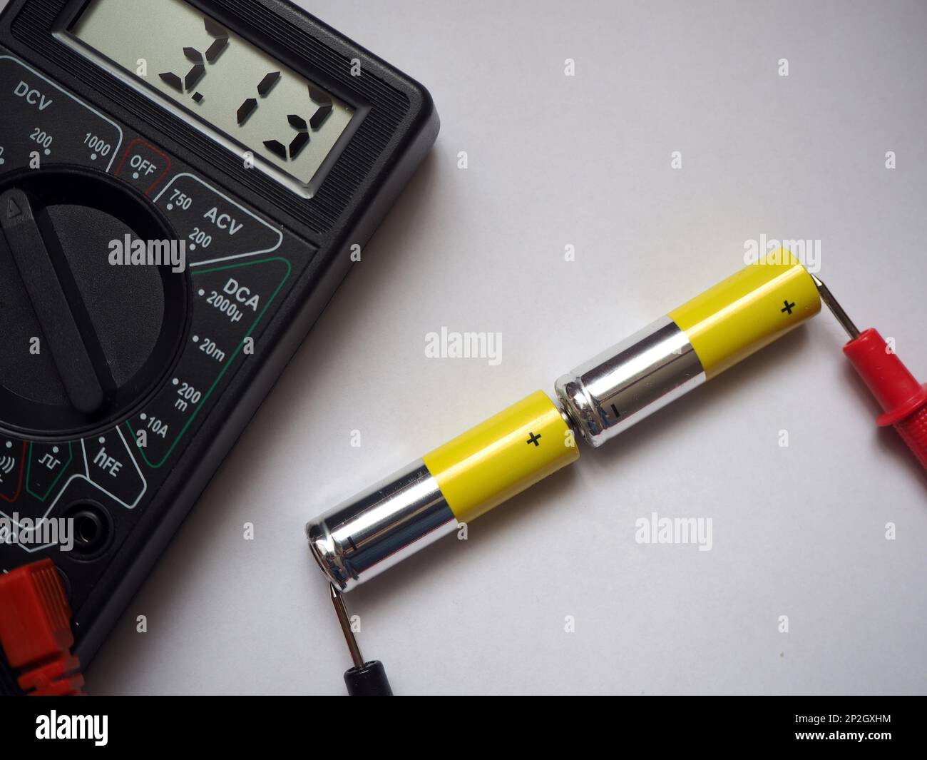 Reading voltage on voltmeter of serial linked two alkaline batteries. AA type cells. Stock Photo