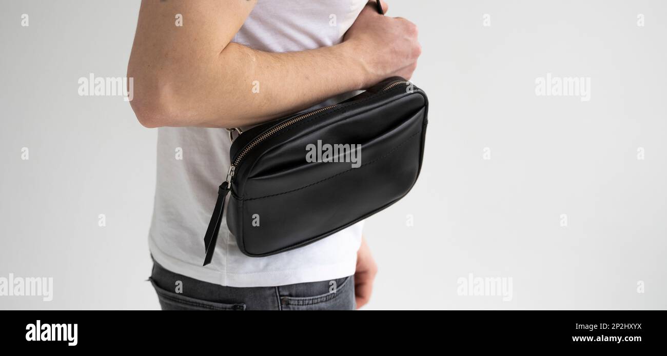 Side view man in a white t-shirt with a leather black handmade bag over his shoulder. Dark designer banana bag. Comfortable small bag for walking. Stock Photo