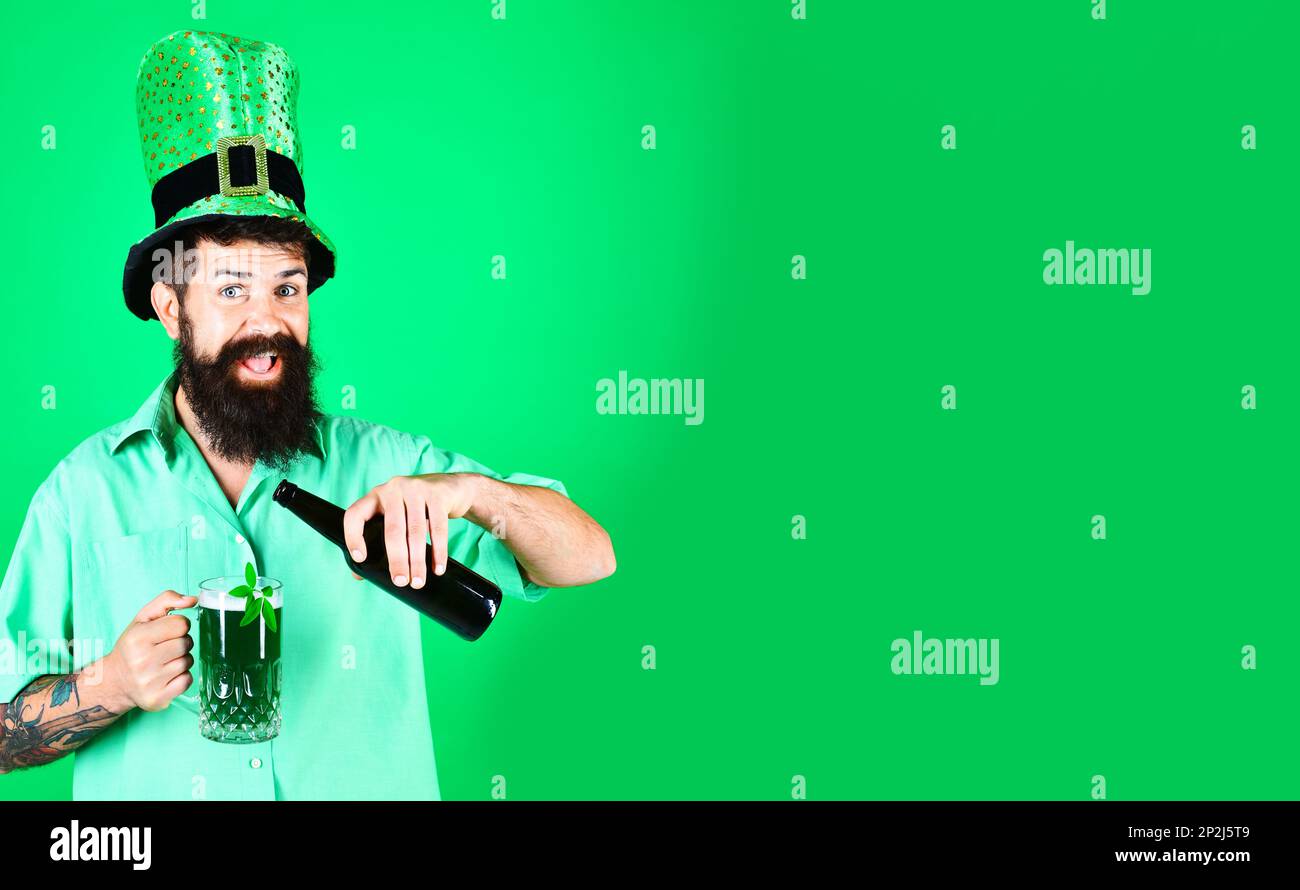 Saint Patricks Day pub party. Happy bearded man in leprechaun hat pouring green beer in glass. Bearded leprechaun with clover in glass of beer. Happy Stock Photo