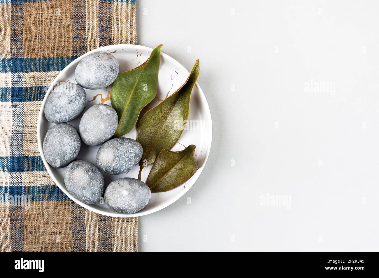 Grey Easter eggs with a sprig and a magnolia leaf on a grey background. Minimalism, copy space, flat lay Stock Photo