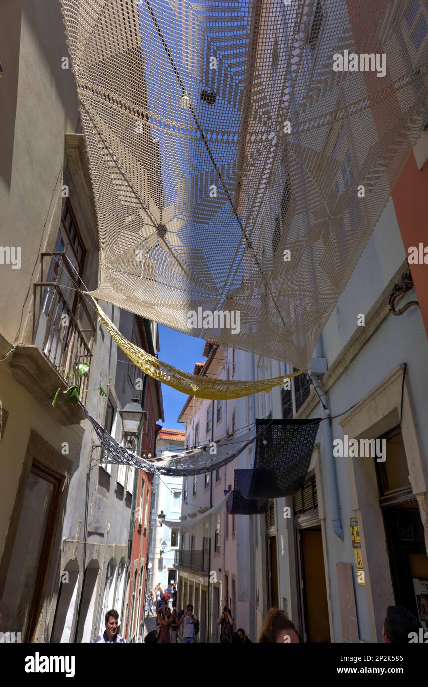 Coimbra, Portugal - August 15, 2022: Street view showing narrow alleyway with woven shades hung between buildings and numerous tourists Stock Photo