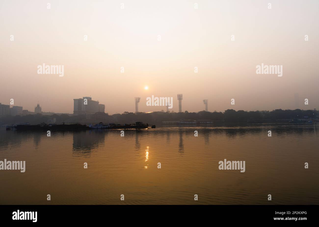 Sun rising in the smoggy atmosphere over the Hooghly River by Eden Gardens cricket stadium at Kolkata (Calcutta), capital city of West Bengal, India Stock Photo