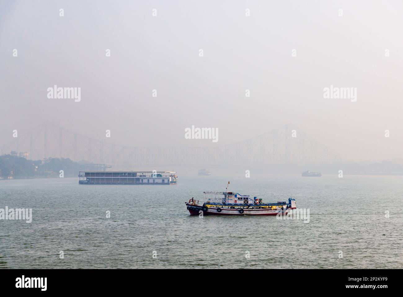 Boats by the Howrah Bridge in early morning smoggy atmosphere over the Hooghly River at Kolkata (Calcutta), capital city of West Bengal, India Stock Photo